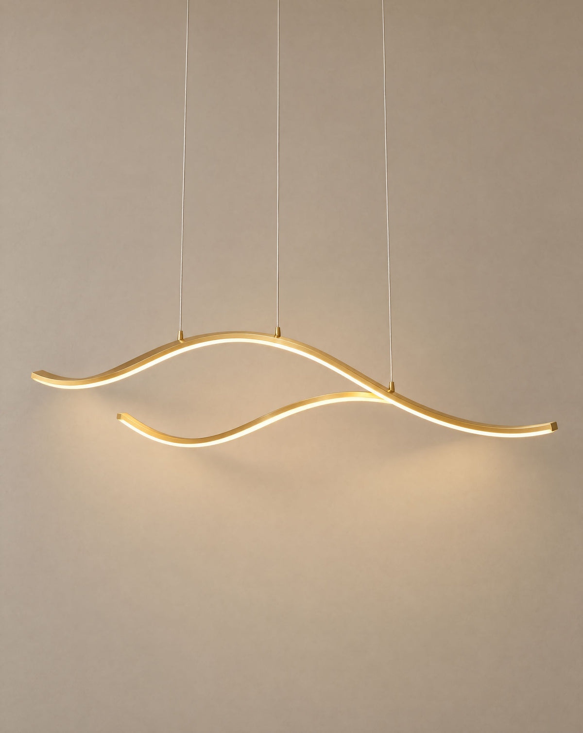 Solsence Crescent gold wave LED pendant light lit with warm 3000K glow in front of a greige wall