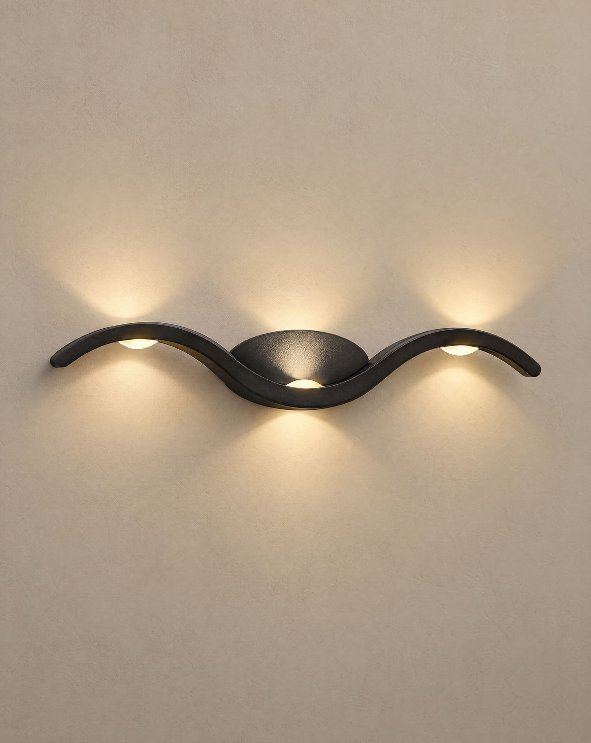 Solsence Tidal black wave wall sconce lit with warm 3000K glow on a greige wall