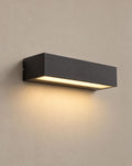 SCI Lighting Lintel black rectangular LED porch wall light lit with warm 3000K glow on a greige wall