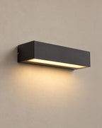 SCI Lighting Lintel black rectangular LED porch wall light lit with warm 3000K glow on a greige wall