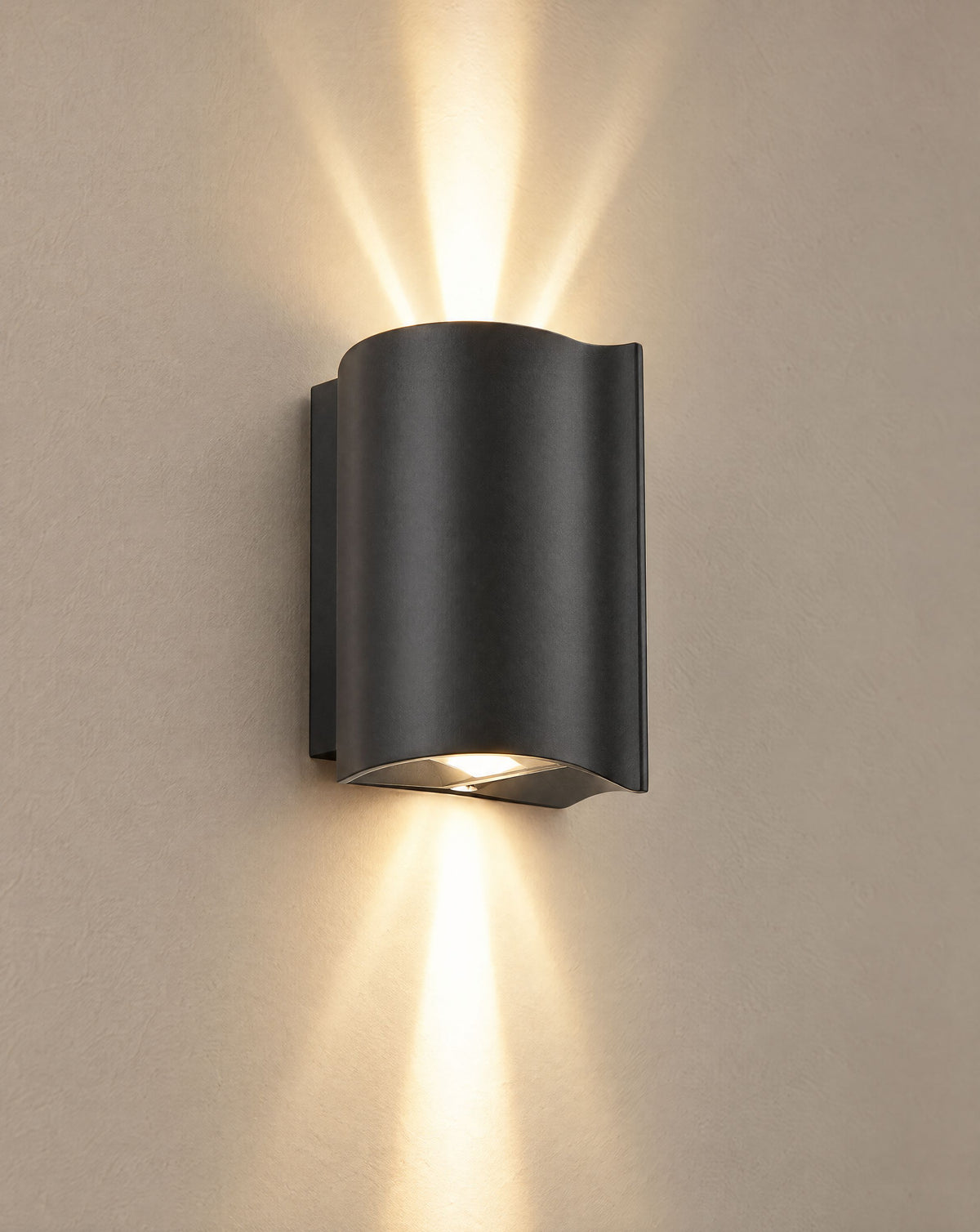 Solsence Onda black up-down LED outdoor wall light lit with warm 3000K glow on a greige wall